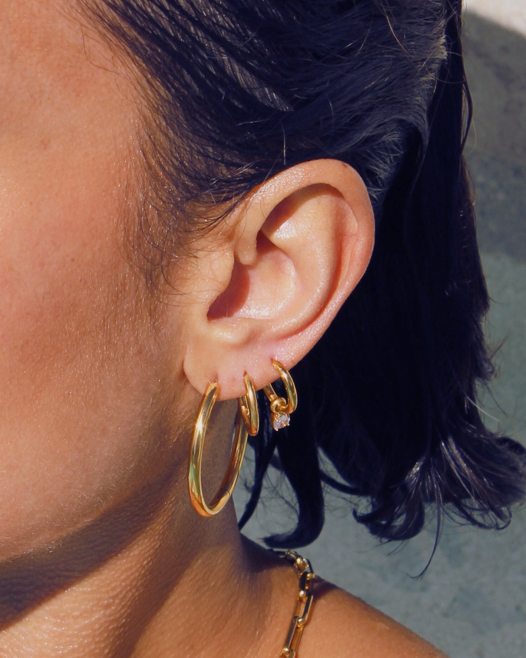 Close-up of an ear wearing waterproof 18k gold hoop earrings with a blurred background