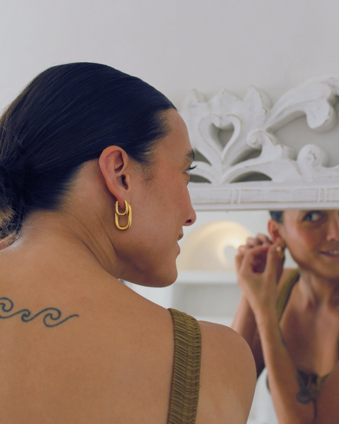 Woman wearing gold hoop earrings with a white decorative mirror in the background