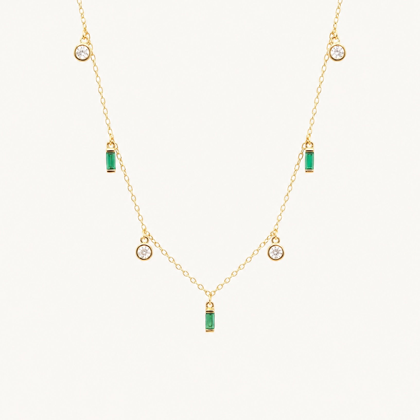 Studio view of the Hunter Rose Maisie 18k gold plated necklace featuring round clear stones and green baguette stones.