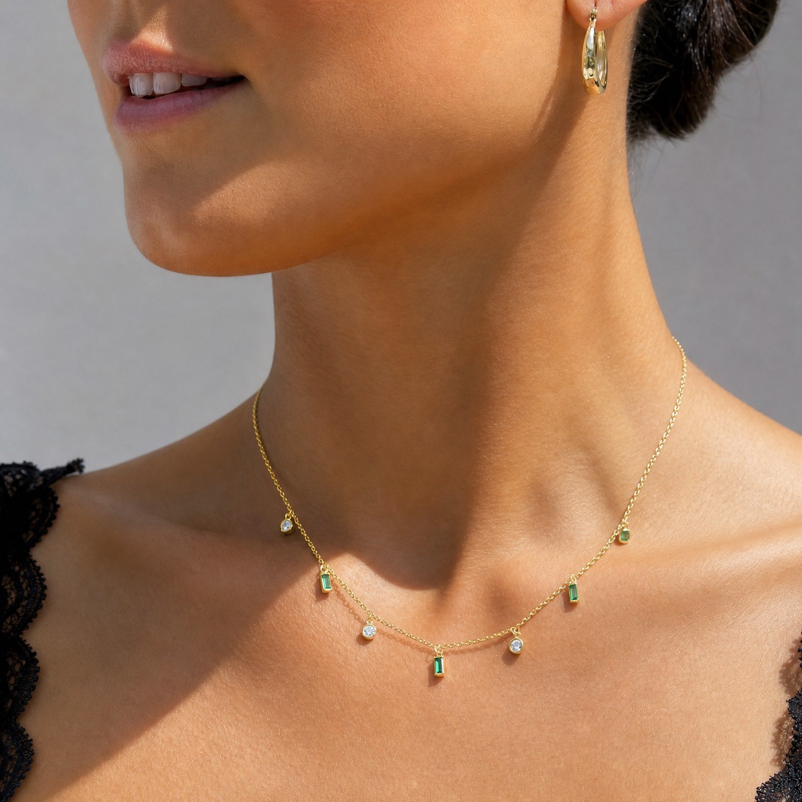Close-up of a model wearing a black lace top and the Hunter Rose Maisie 18k gold plated green stone necklace.