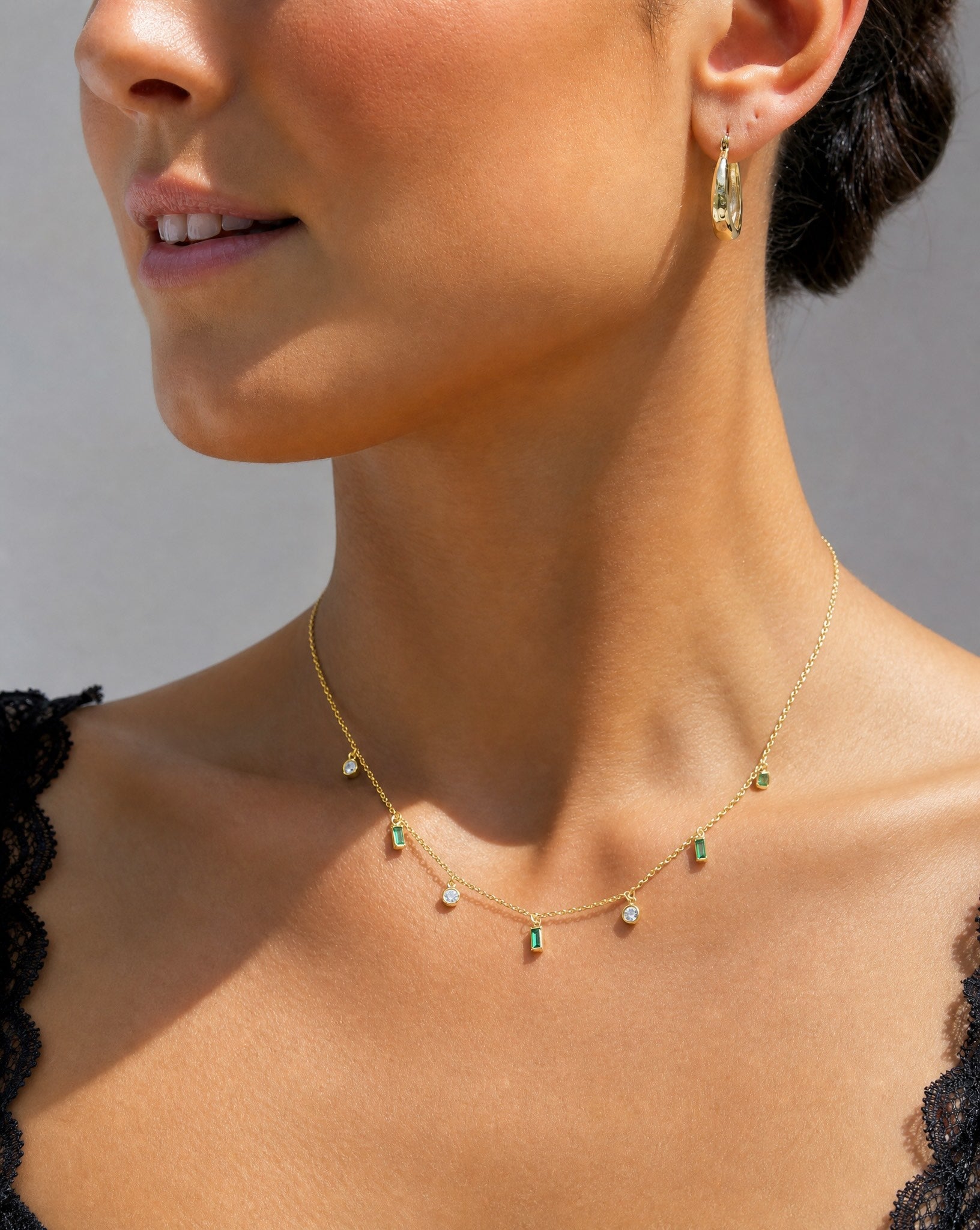 Close-up of a model wearing a black lace top and the Hunter Rose Maisie 18k gold plated green stone necklace.