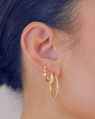 Gold drop stud earrings with a small gemstone worn by a person with black air.