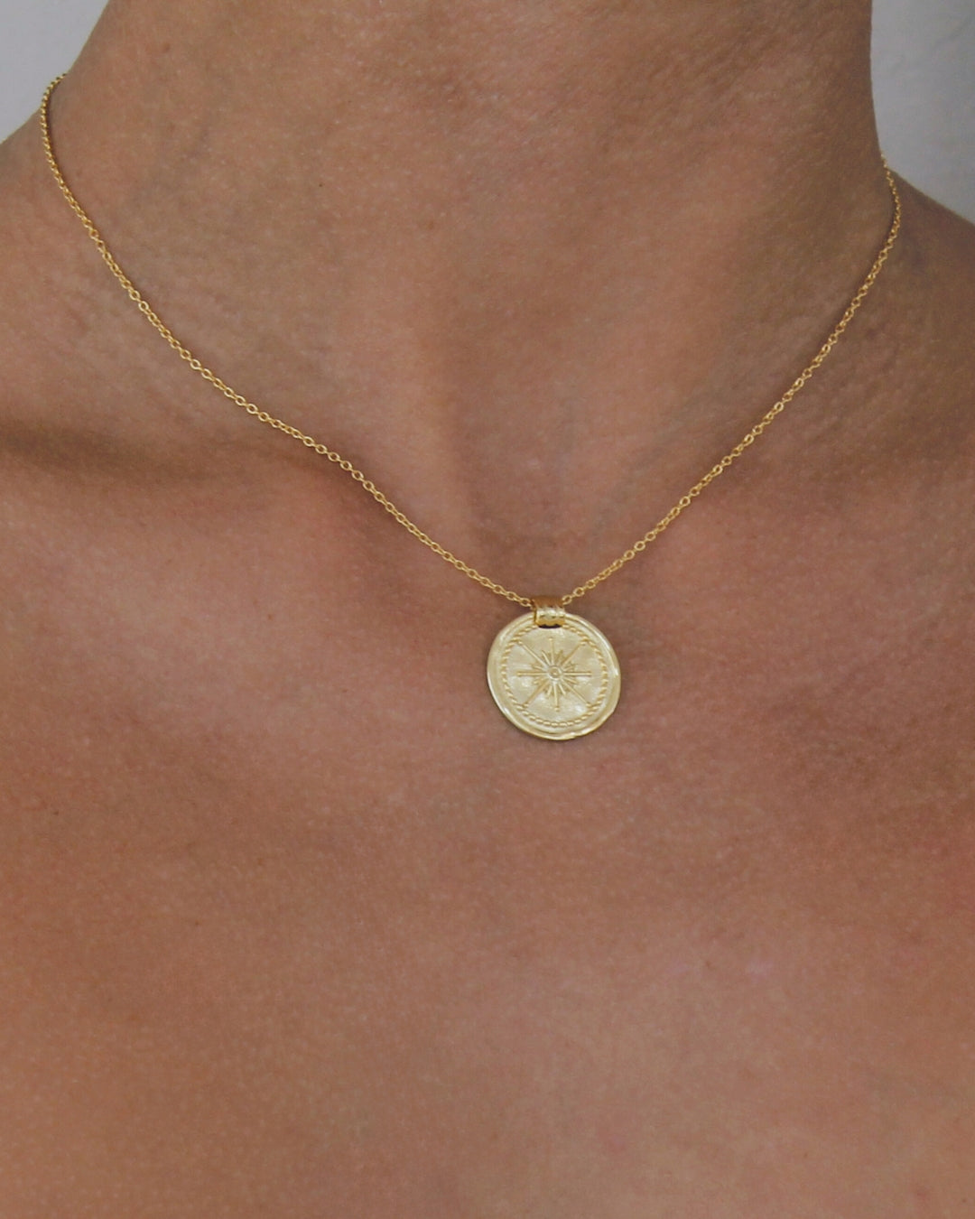 18 carat Gold necklace with a round pendant on a person's neck against a neutral background