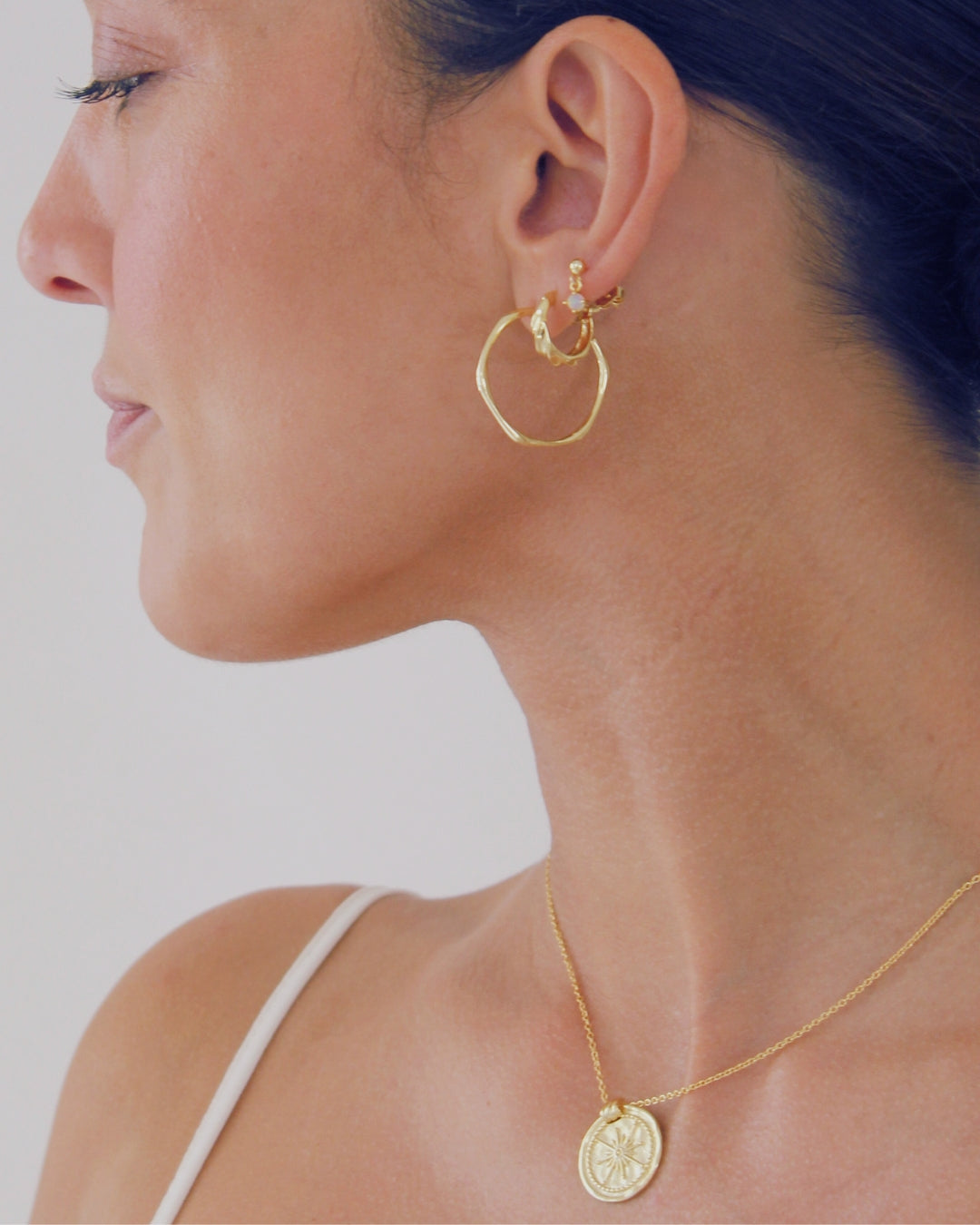 Close-up of a person wearing gold hoop earrings and a necklace with a coin pendant.