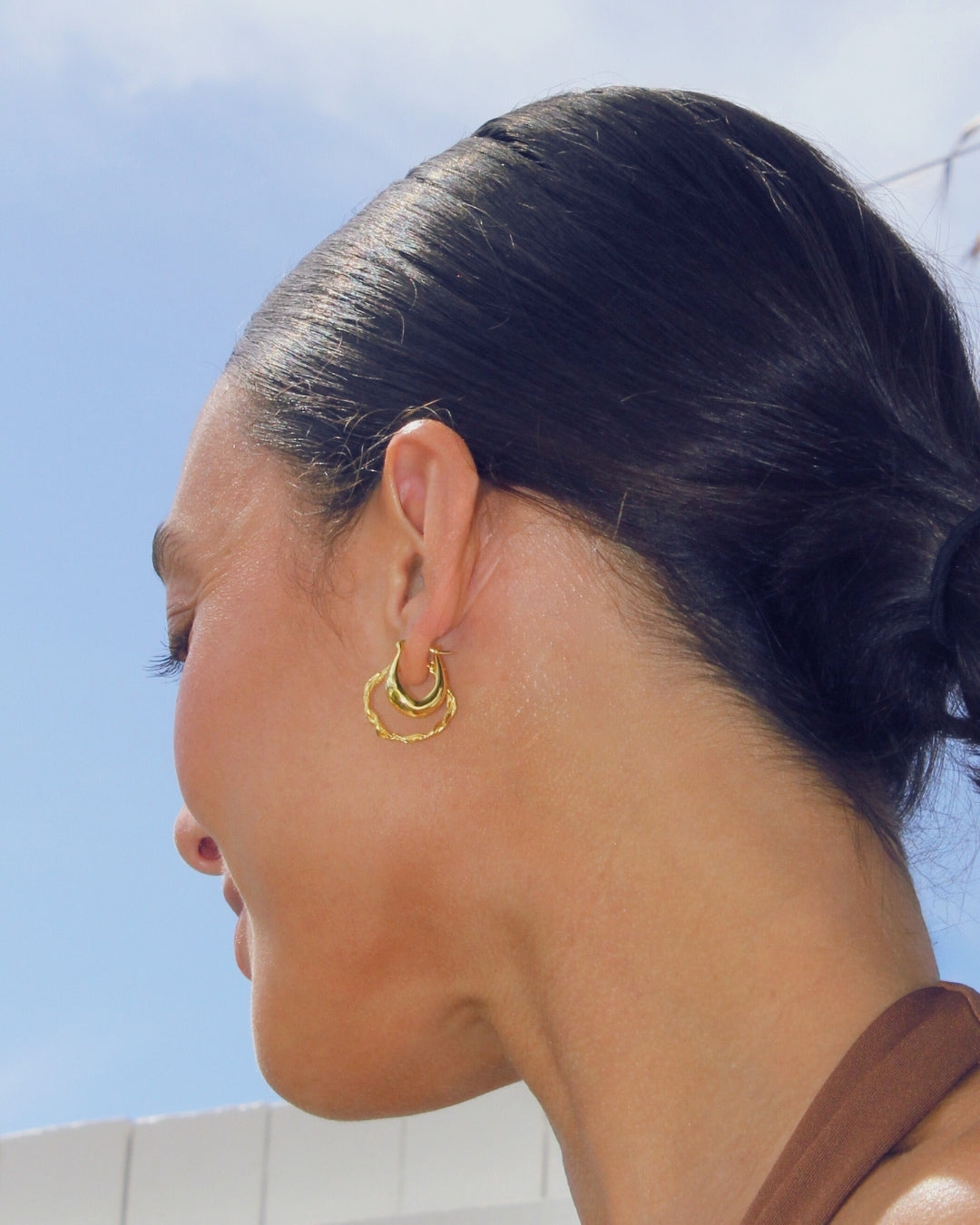 Close-up of a person wearing gold hoop earrings with a clear blue sky background