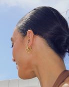 Close-up of a person wearing gold hoop earrings with a clear blue sky background