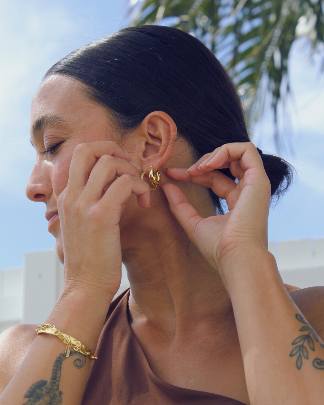 Woman adjusting a gold earring with a blurred outdoor background
