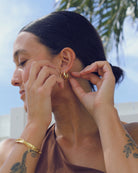 Woman adjusting a gold earring with a blurred outdoor background