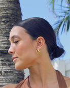 Woman with a bun wearing gold earrings, palm tree in the background