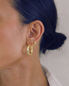 Close-up of an ear wearing gold hoop earrings  and the Freya chain earring with a blurred background