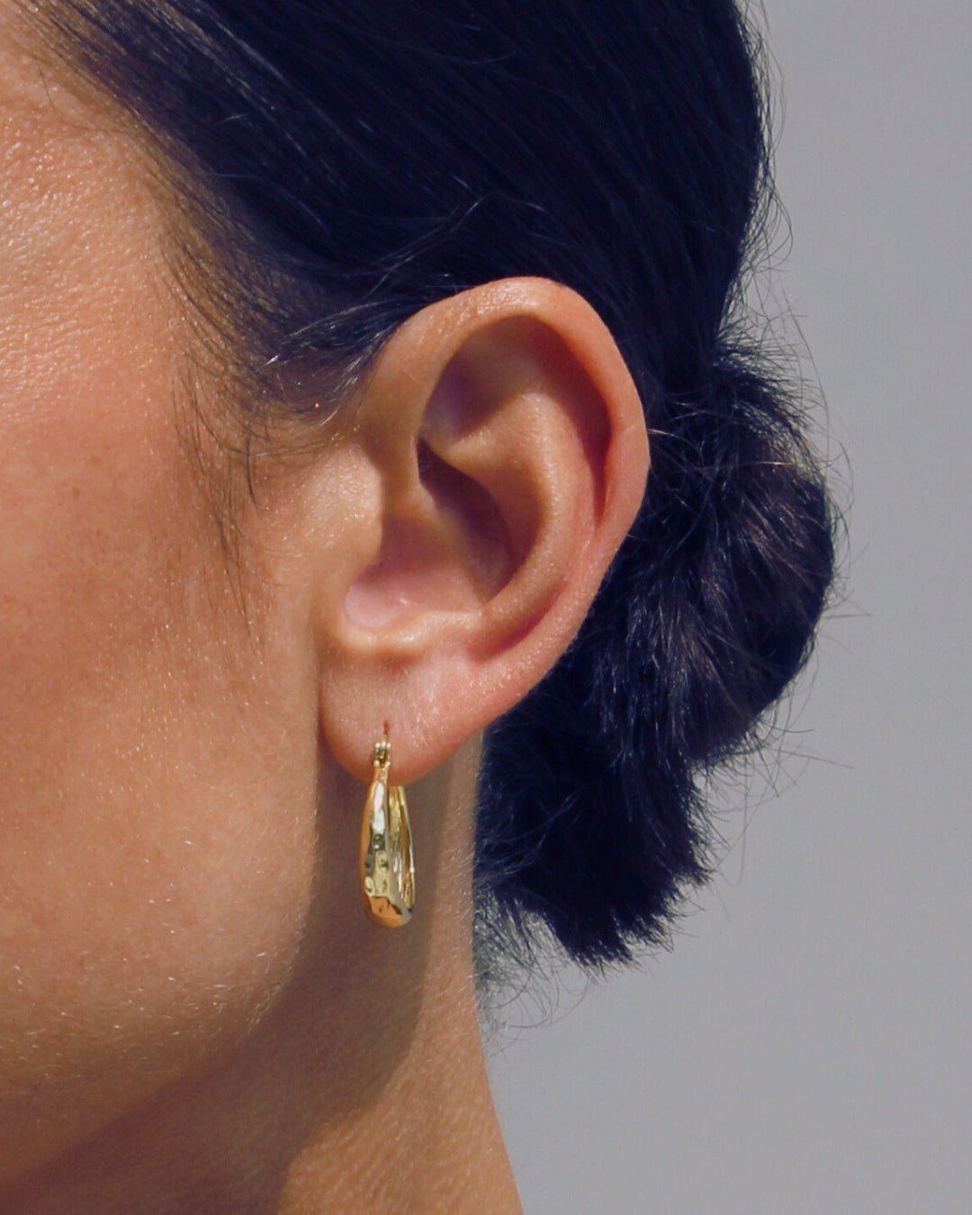 Close-up of an ear wearing a gold earring with a blurred background