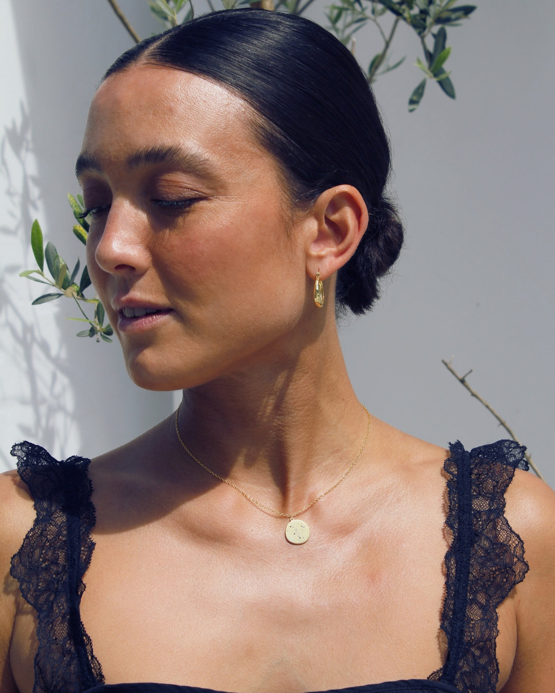 Woman wearing a black lace top with gold  hoop earrings and a gold pendant necklace.