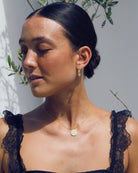 Woman wearing a black lace top with gold  hoop earrings and a gold pendant necklace.