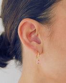 Gold Pendant hoop earring with a pink gemstone worn by a person with brown hair.