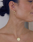 Close-up of a person wearing gold hoop earrings and a necklace with a coin pendant.