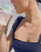 Person holding a Perrier glass with a blurred background and gold jewellery