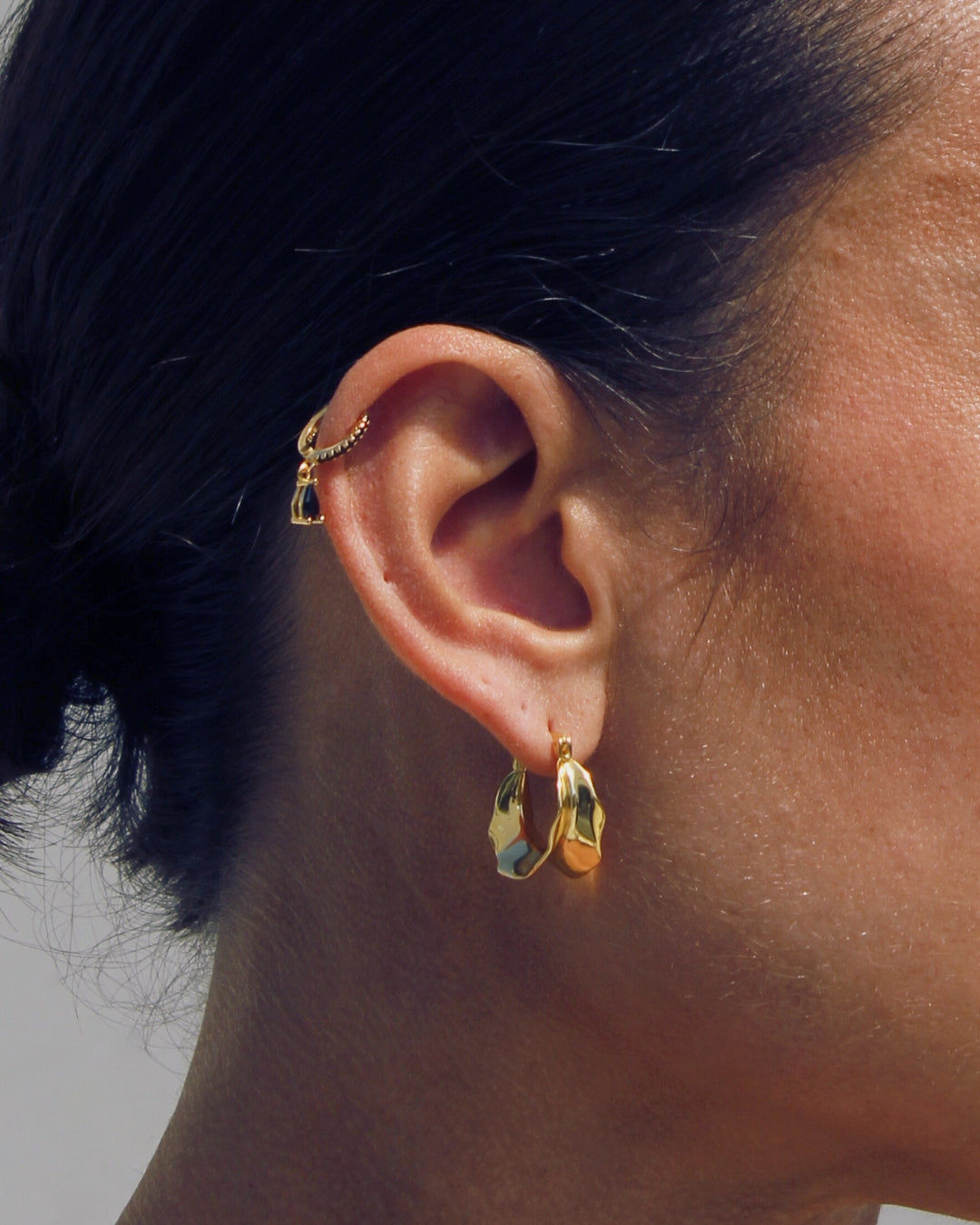 Close-up of an ear wearing gold hoop earrings with a neutral background