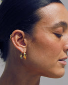 Close-up of a woman wearing  the Stella 18k gold hoop earrings with a neutral background
