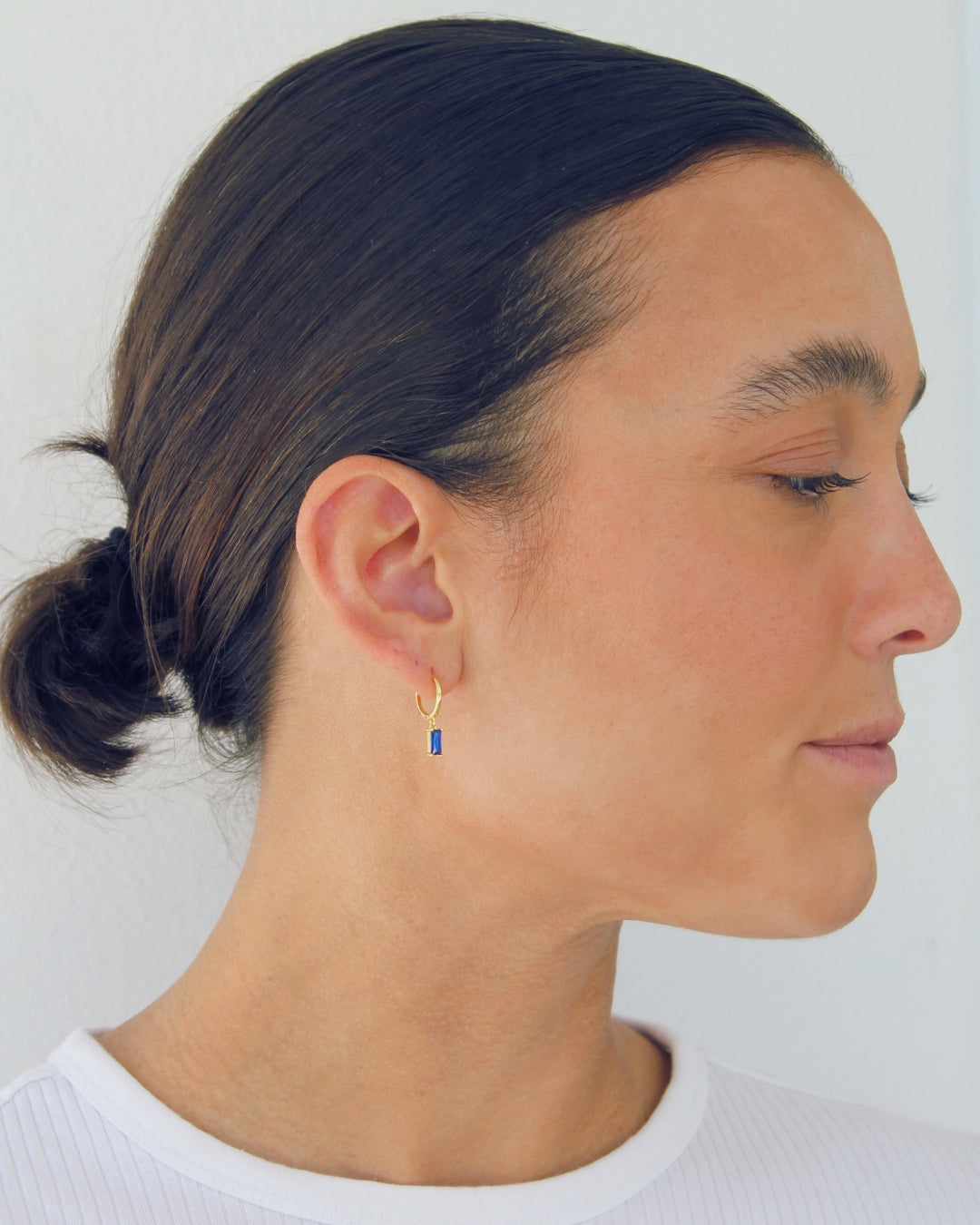 Person wearing a gold pendant hoop earring with a blue gemstone on a plain background