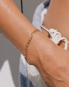 Gold  Figaro chain bracelet on a wrist with a blurred background