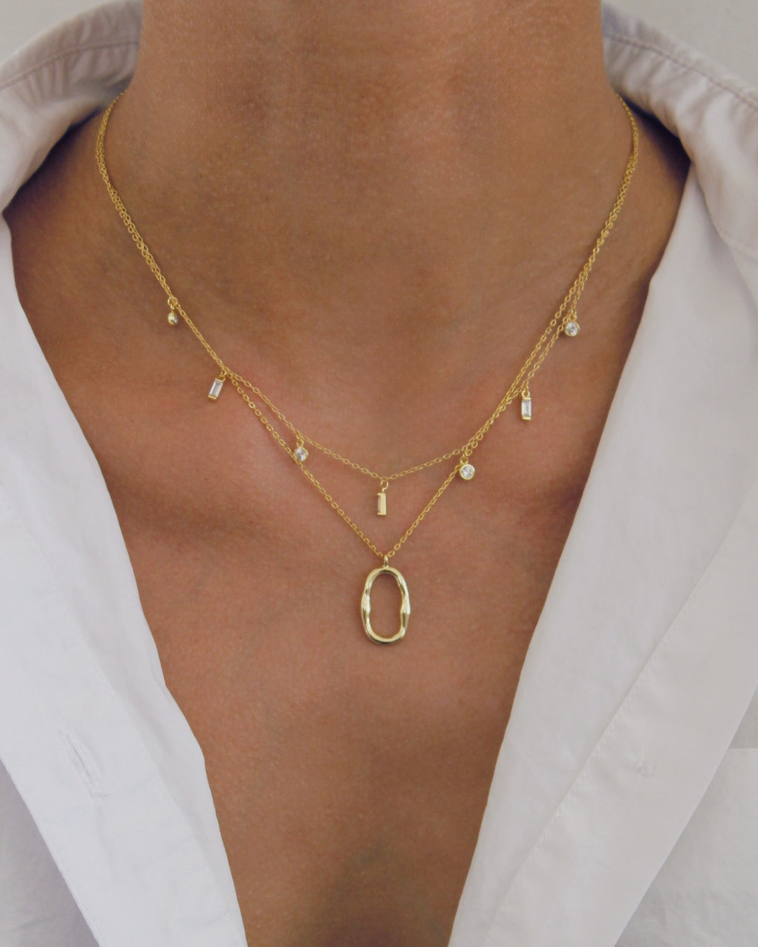 Gold necklace with a pendant on a person wearing a light-colored shirt.