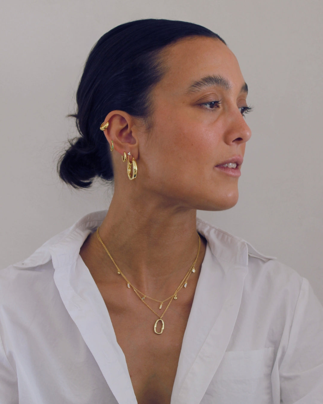 Woman wearing gold earrings and necklaces against a plain background