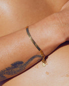 Gold waterproof snake chain bracelet on a wrist with a tattoo on the skin