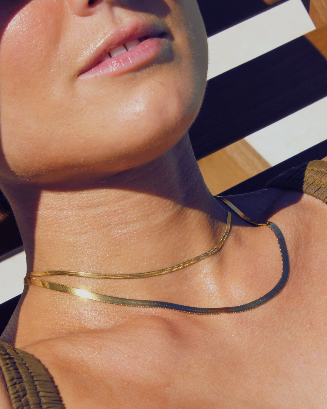Close-up of a person wearing a gold snake chain necklace laying on pool recliner