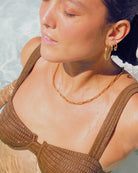 Woman wearing a brown bikini with gold waterproof jewellery, standing in clear water.