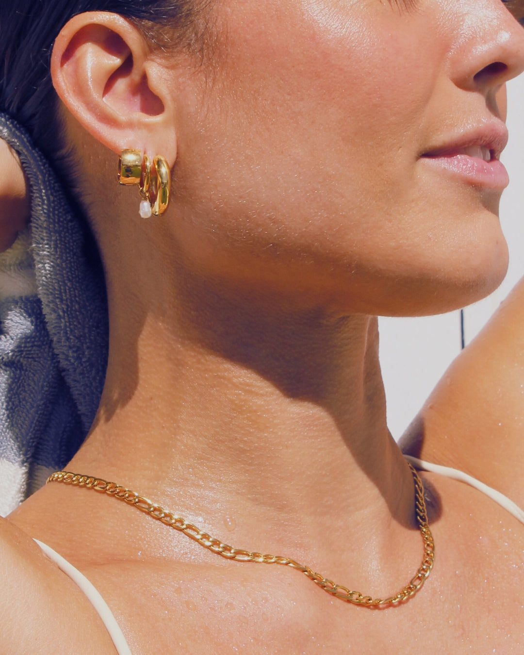 Close-up of a person wearing gold earrings and a gold  figaro chain necklace.