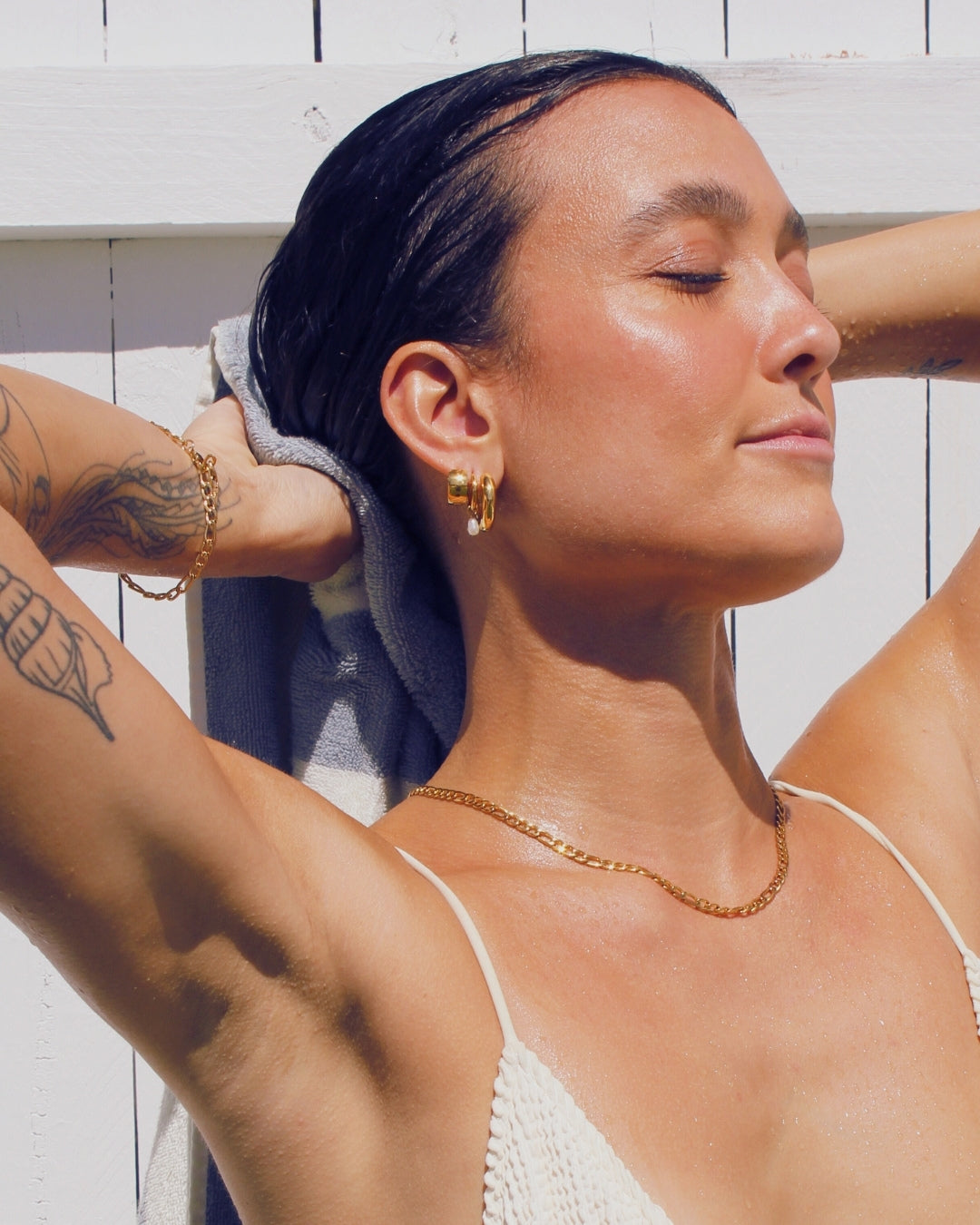 Woman with tattoos and waterproof gold jewellery against a white wooden background