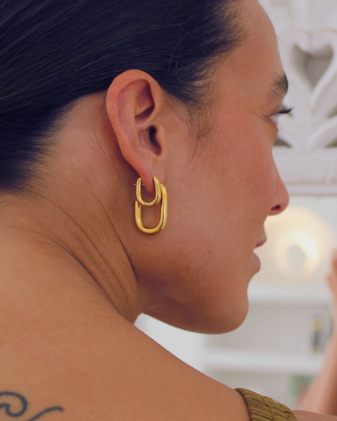 Close-up of a person wearing  gold hoop earrings with a blurred background
