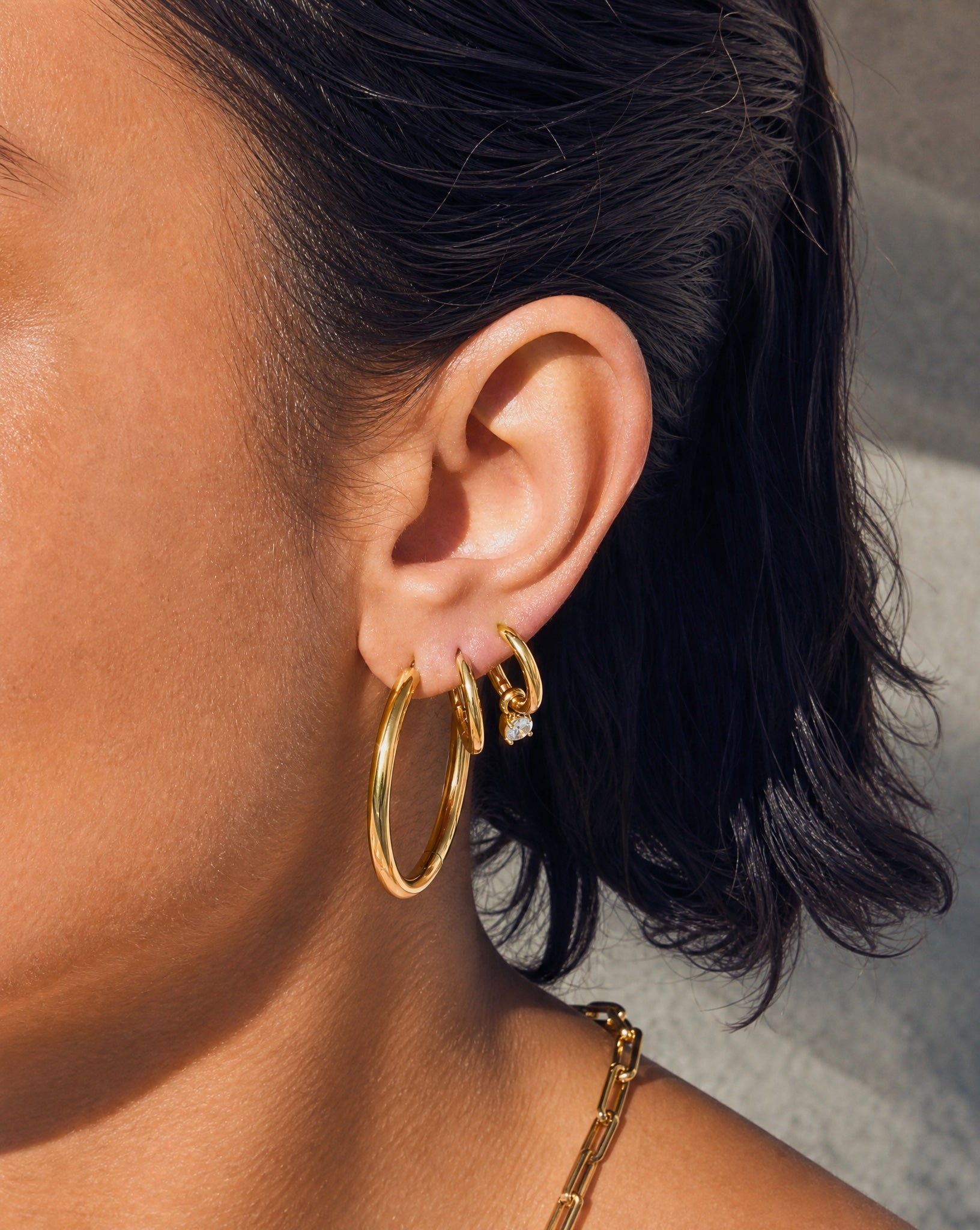 Close-up on the ear showing the tarnish-free Chloe 18k gold hoops layered with other waterproof jewellery by Hunter Rose.