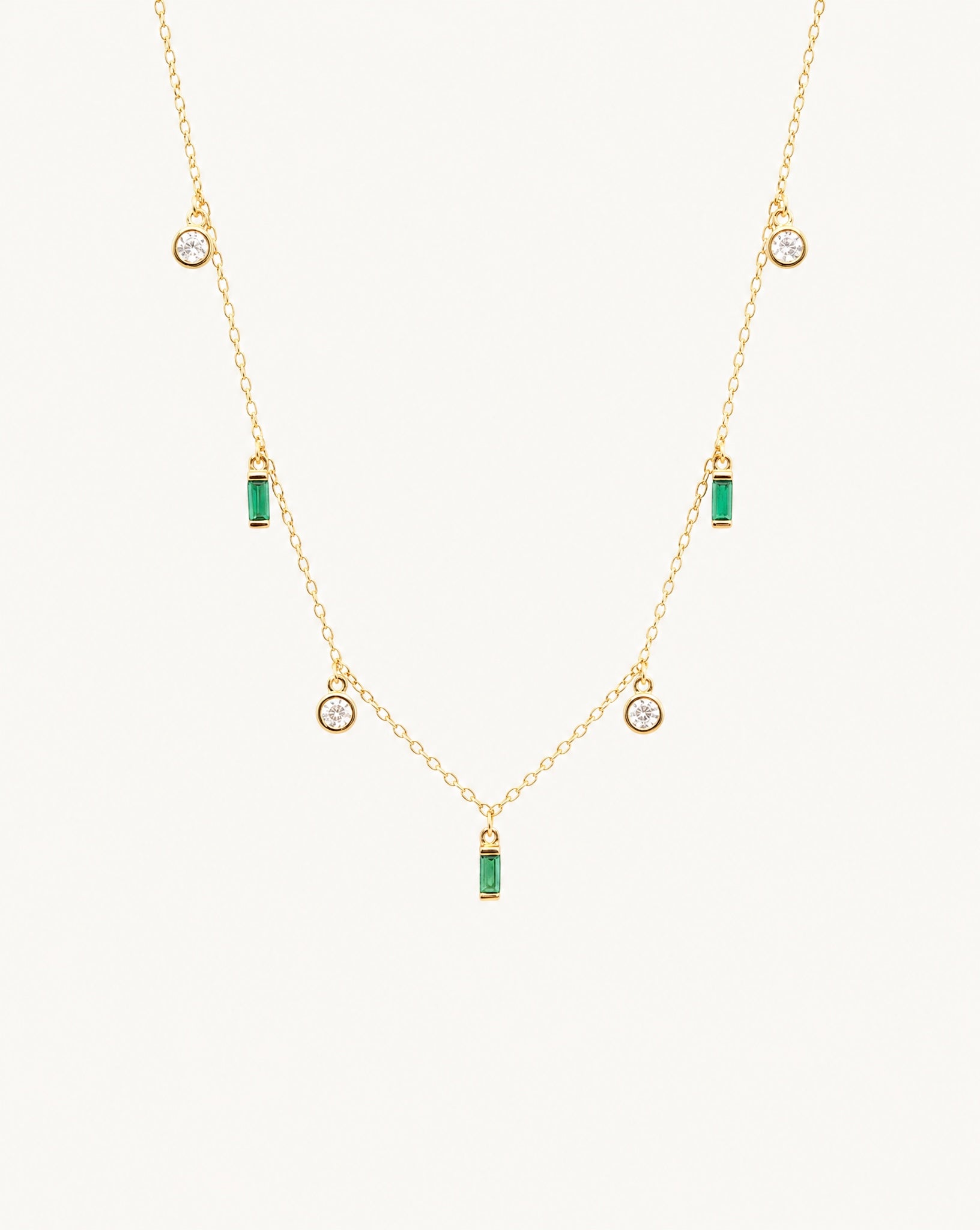 Studio view of the Hunter Rose Maisie 18k gold plated necklace featuring round clear stones and green baguette stones.